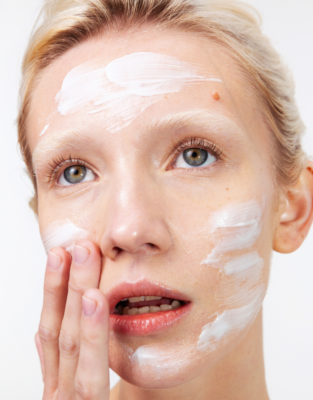 Close-up of a girl applying Common Clouds Cloud Barrier cream to their face with a neutral background.