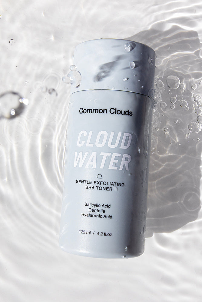 Common Clouds Cloud Water – gentle exfoliating BHA toner with salicylic acid, centella and hyaluronic acid, photographed with water droplets.