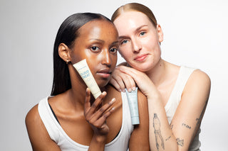 Two women holding skincare products against a plain background