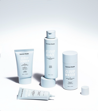 A set of five Common Clouds skincare bottles and tubes in a clean studio arrangement. The products include Cloud Screen, Cloud Glaze, Cloud Water, and Cloud Milk, all in a uniform light icy blue color with white text and caps, set against a bright white background with soft shadows.