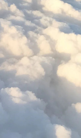 A close-up view of dense white and light gray clouds with soft sunlight filtering through the voluminous formations.