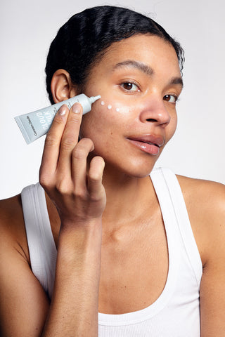 Woman applying cloud milk serum to her face with a white background.