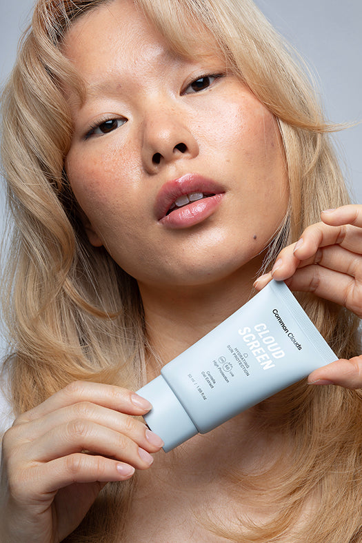 A girl is holding a Cloud Screen spf 50 from Common Clouds. 