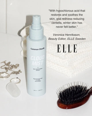 Common Clouds Cloud Mist spray bottle on a white surface next to a hairbrush, jewelry, and a folded towel, with a quote and ELLE branding.