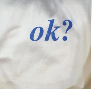 A close-up of a white fabric surface with the word "ok?" printed in blue serif letters.