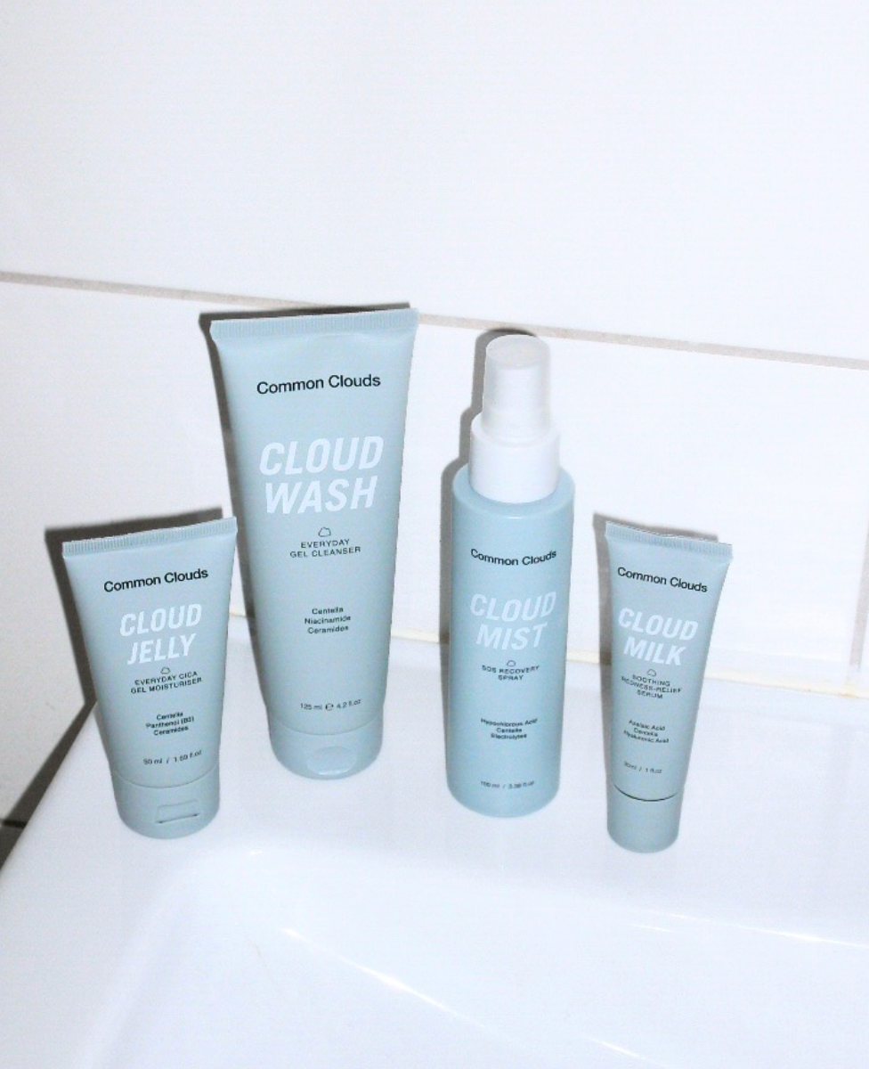 Set of Common Clouds skincare products on a white surface with a tiled wall background.